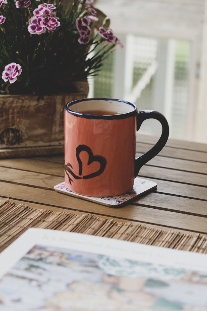 A warm coffee mug with heart design on a rustic wooden table surrounded by flowers, perfect for relaxation.
