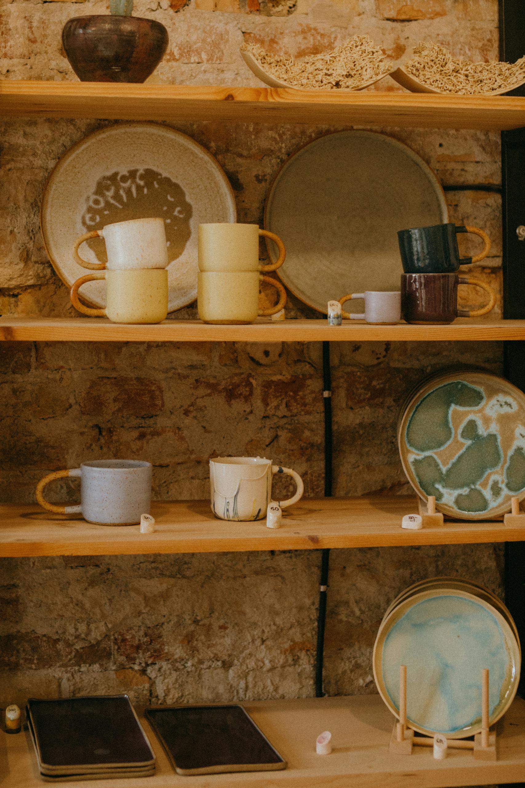 Vibrant ceramic dishware displayed on rustic wooden shelves in workshop setting.